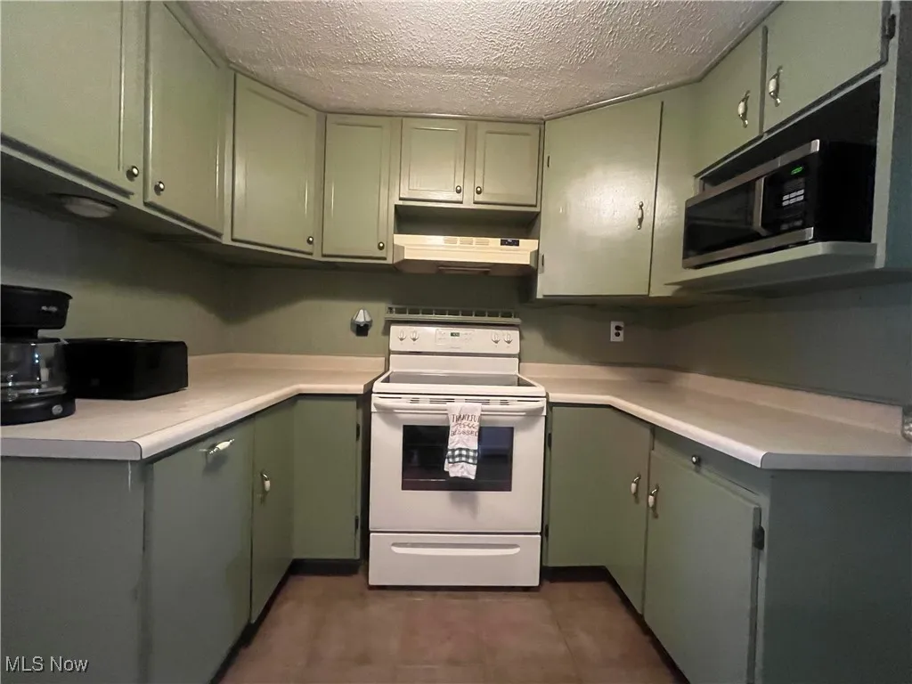 Kitchen with white electric stove, green cabinetry, a textured ceiling, stainless steel microwave, and light countertops