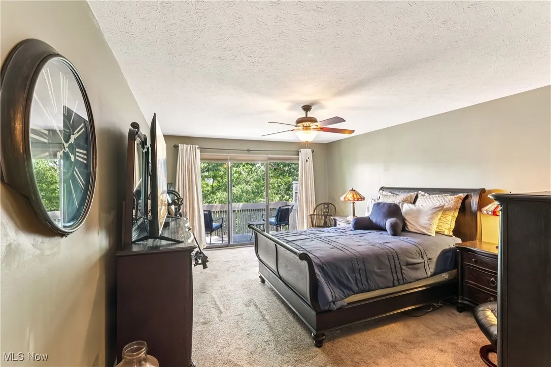 Primary bedroom with sliding glass door out to a balcony, ceiling fan / light and carpet flooring.