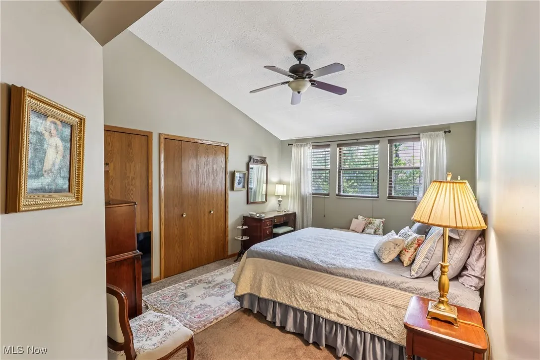 Bedroom featuring vaulted ceiling, ceiling fan / light, double closets, and carpet flooring