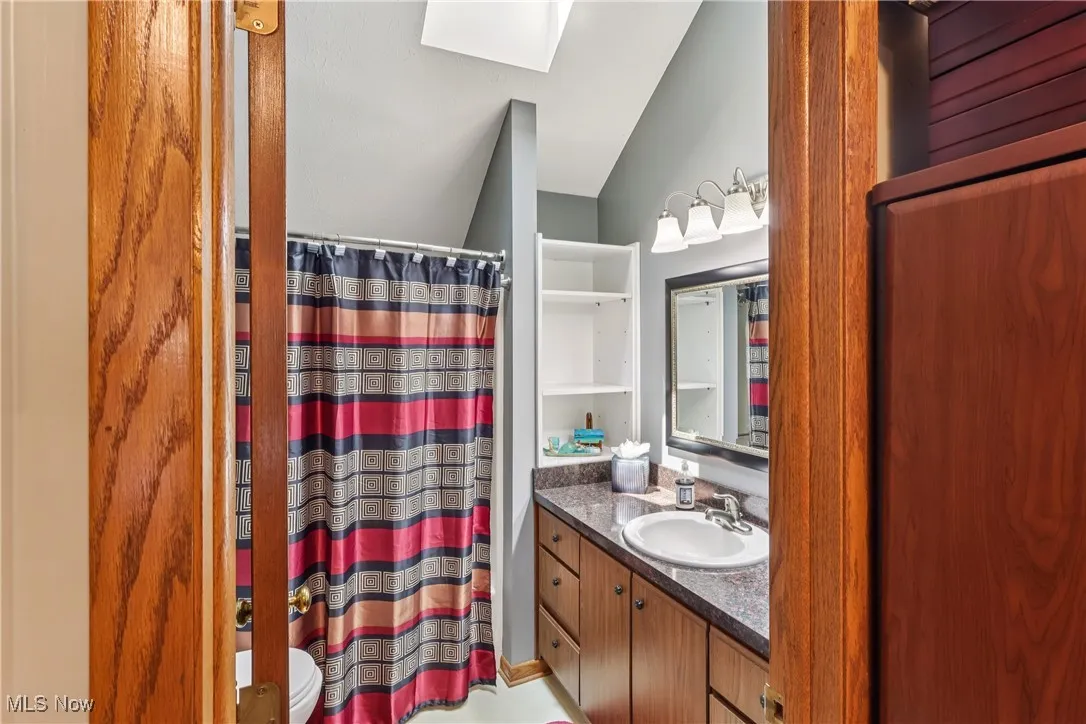 Second floor bathroom with vaulted ceiling, sky light, sink, vanity, shower / tub combo, commode and ceramic flooring