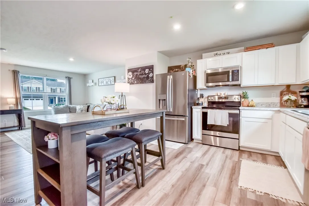 Kitchen with stainless steel appliances, white cabinetry, light wood-style floors, open shelves, and a breakfast bar