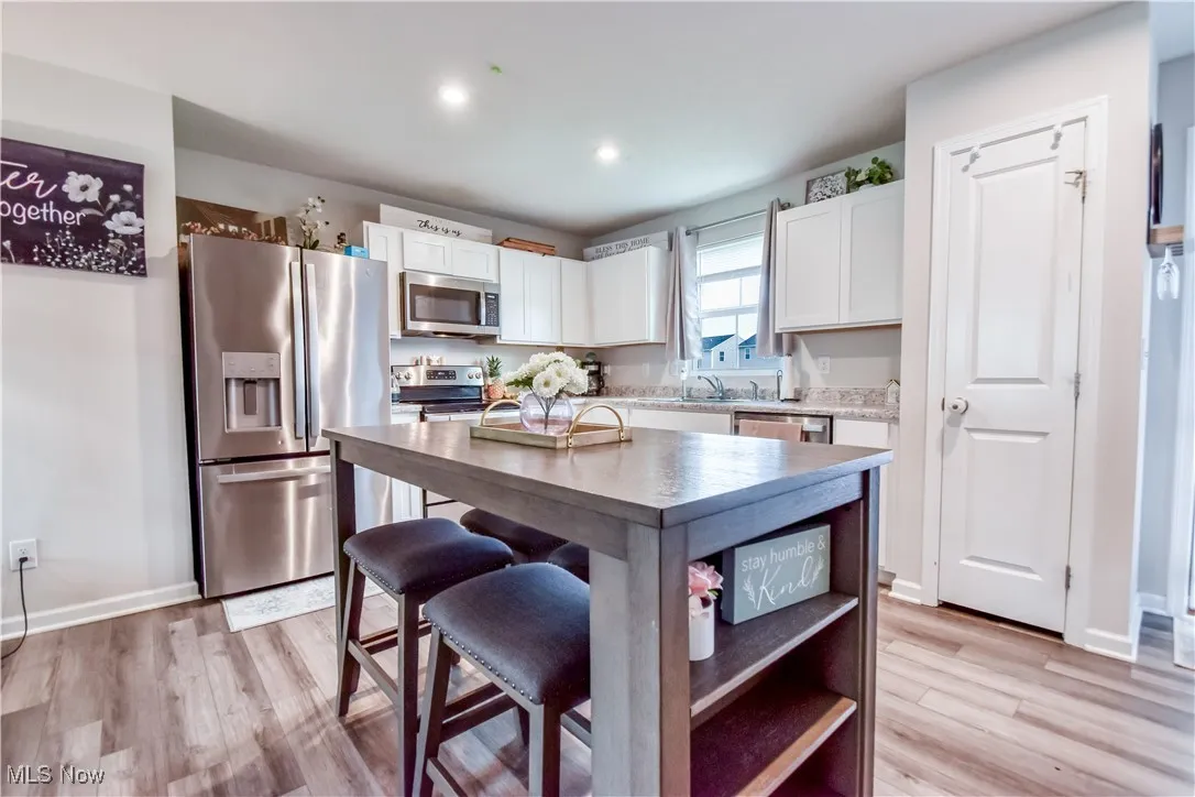 Kitchen with appliances with stainless steel finishes, white cabinets, light wood finished floors, light countertops, and recessed lighting