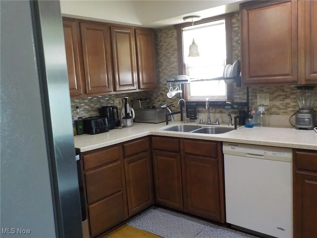Kitchen featuring white dishwasher, freestanding refrigerator, decorative backsplash, and light countertops