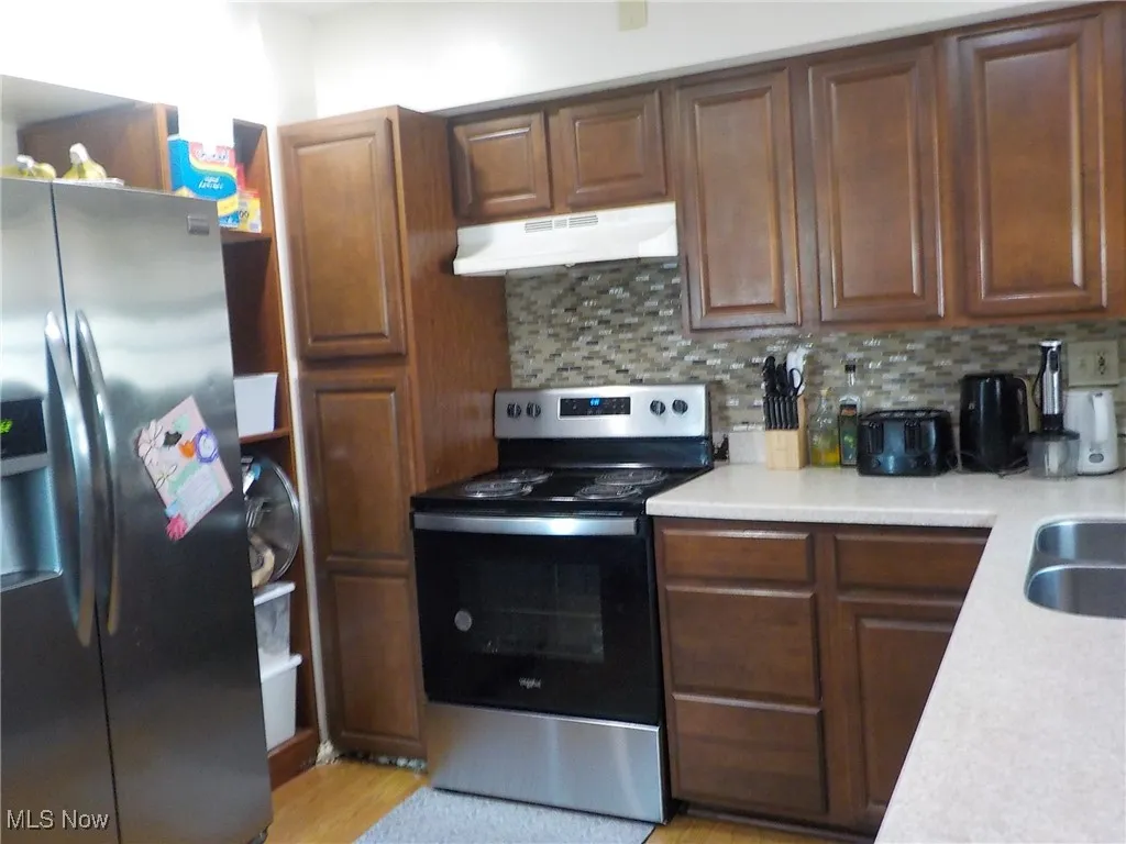 Kitchen featuring stainless steel appliances, light countertops, under cabinet range hood, and backsplash