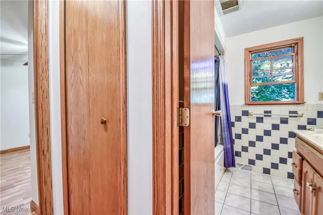 Bathroom featuring vanity, tile walls, tile patterned flooring, shower / tub combo with curtain, and wainscoting