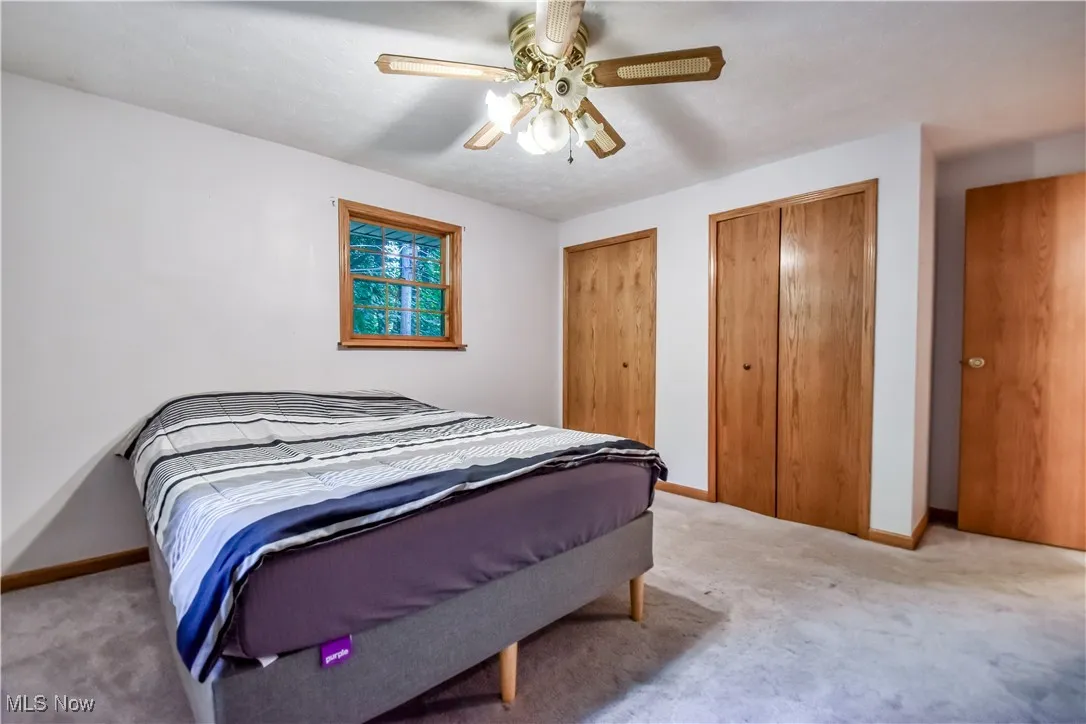Carpeted bedroom with multiple closets and a ceiling fan