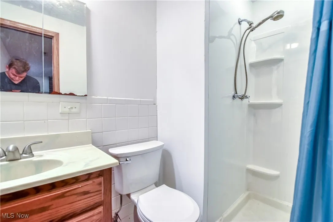 Full bath featuring a stall shower, vanity, and tile walls