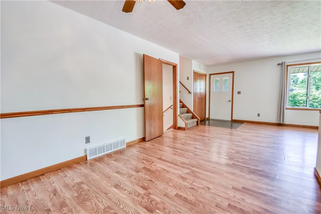 Unfurnished room featuring a textured ceiling, wood finished floors, stairway, and a ceiling fan