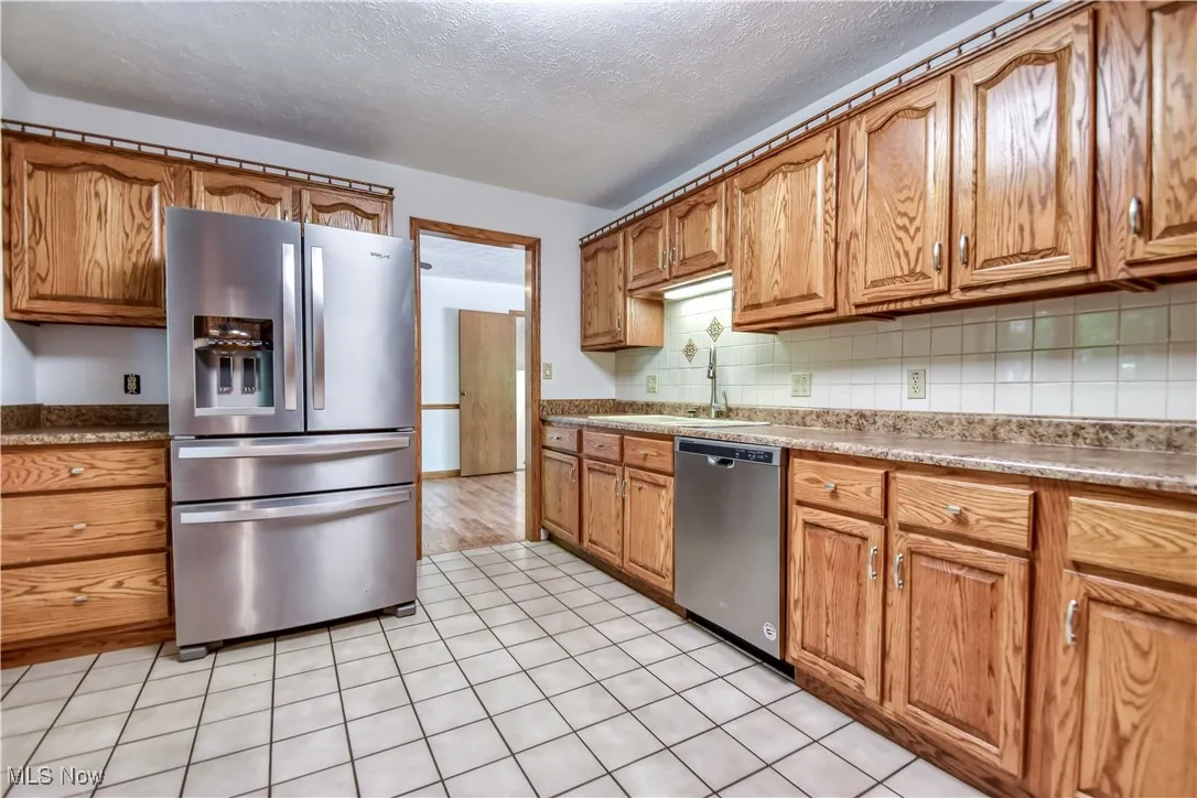 Kitchen featuring appliances with stainless steel finishes, brown cabinets, a textured ceiling, and decorative backsplash