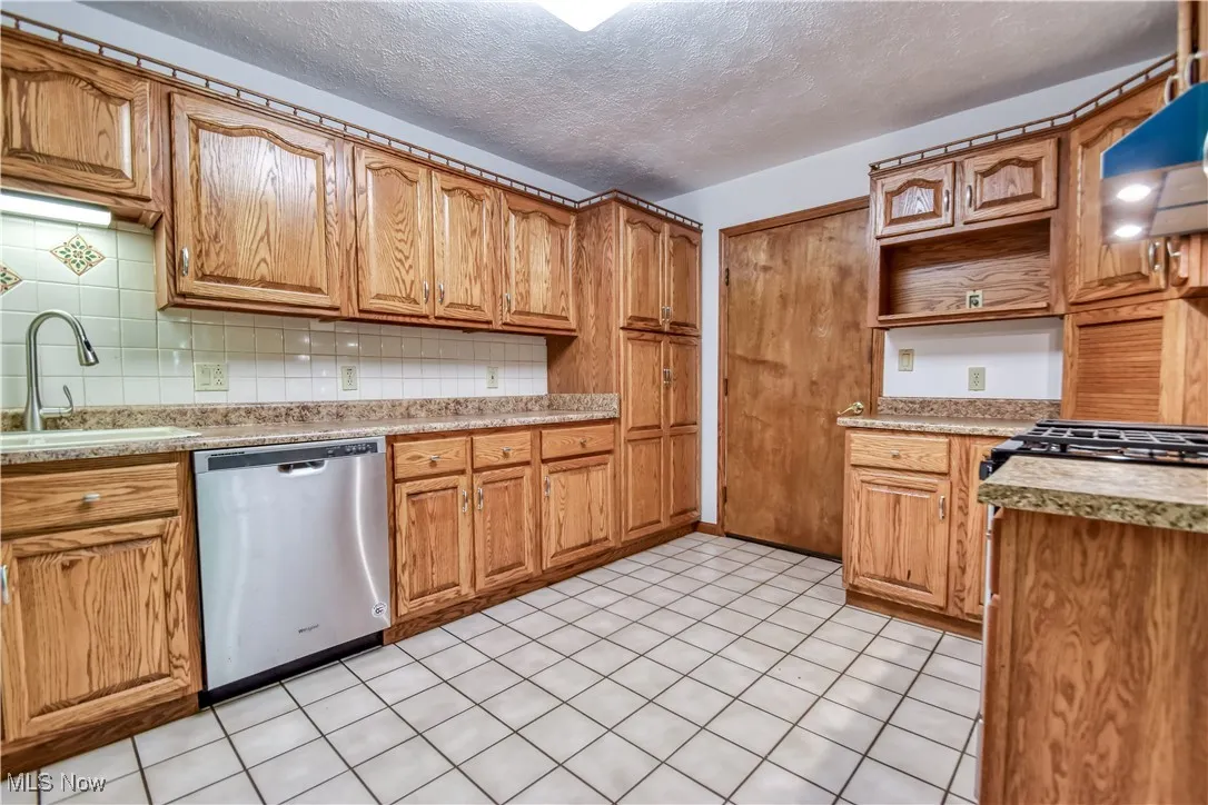 Kitchen featuring dishwasher, open shelves, tasteful backsplash, range hood, and a textured ceiling