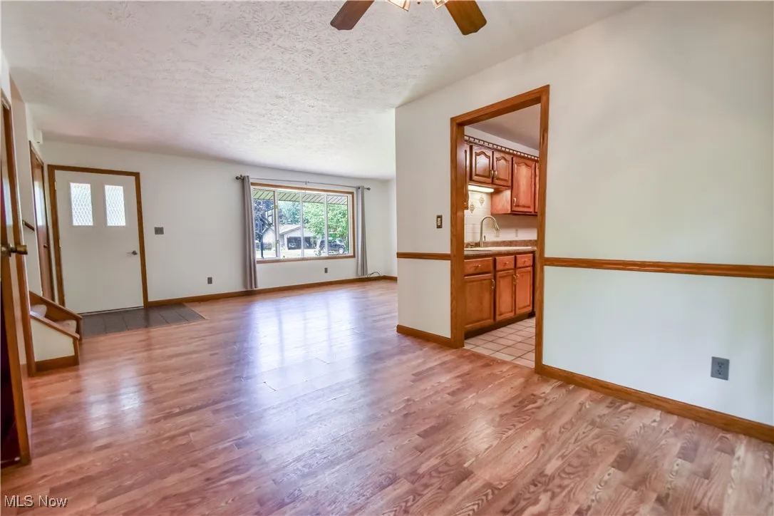 Unfurnished living room with plenty of natural light, ceiling fan, light wood finished floors, and a textured ceiling