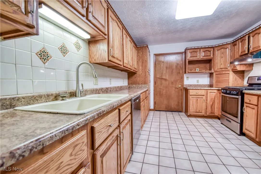 Kitchen with stainless steel appliances, backsplash, a textured ceiling, under cabinet range hood, and light tile patterned flooring