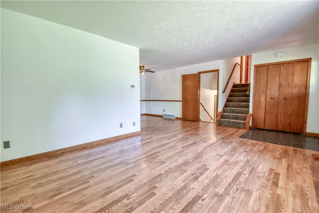 Unfurnished living room featuring light wood-style flooring, stairway, a textured ceiling, and a ceiling fan
