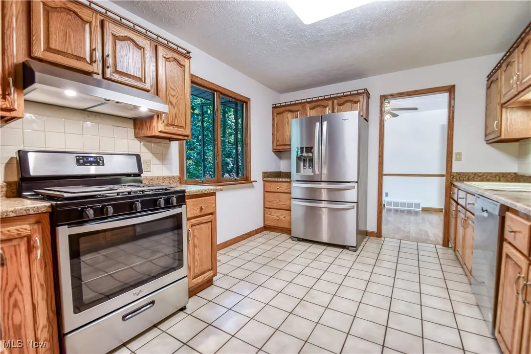Kitchen featuring stainless steel appliances, under cabinet range hood, decorative backsplash, a textured ceiling, and light countertops