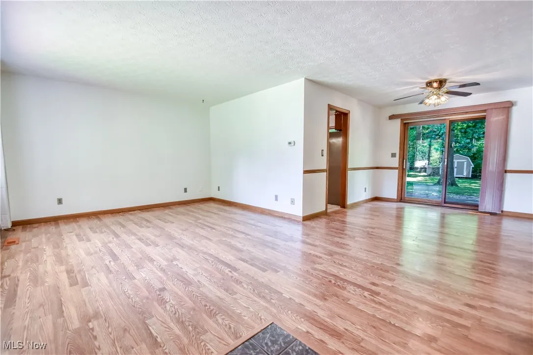 Unfurnished living room with light wood-type flooring, ceiling fan, and a textured ceiling