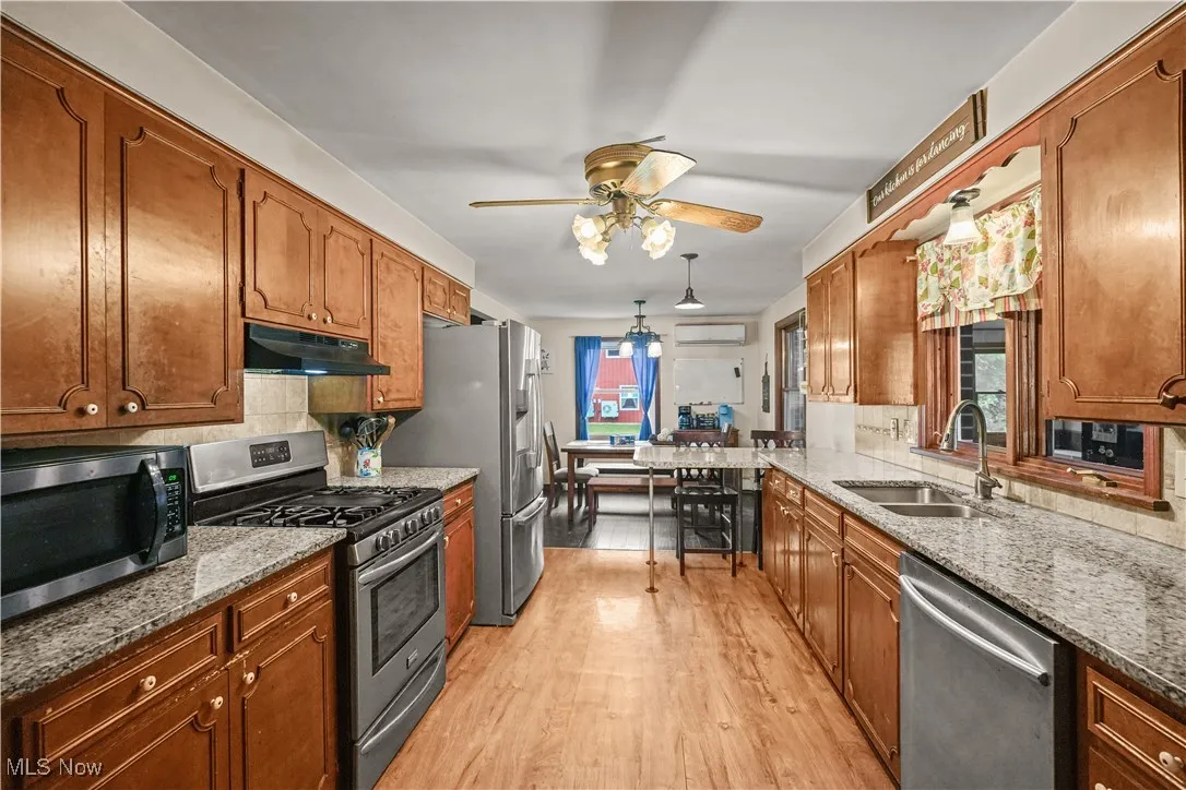 Kitchen featuring stainless steel appliances, ceiling fan, light wood-type flooring, backsplash, and brown cabinetry