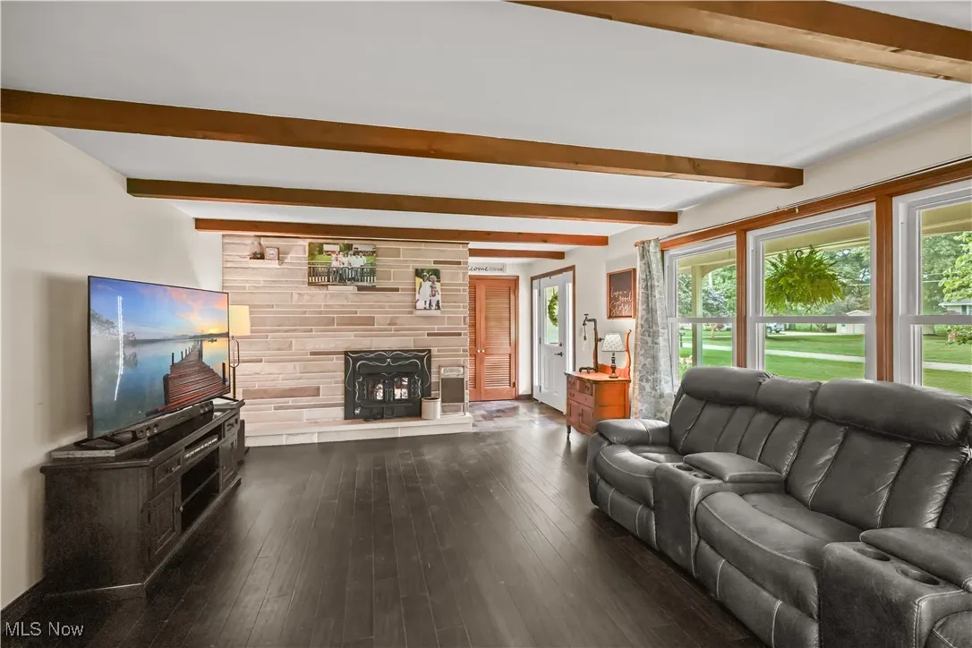 Living area with beam ceiling, dark wood-style floors, and a fireplace