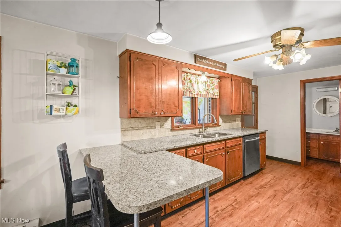 Kitchen featuring decorative backsplash, ceiling fan, brown cabinets, stainless steel dishwasher, and light wood-style floors