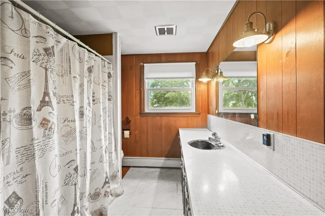Bathroom featuring wood walls, vanity, marble finish flooring, baseboard heating, and a shower with shower curtain
