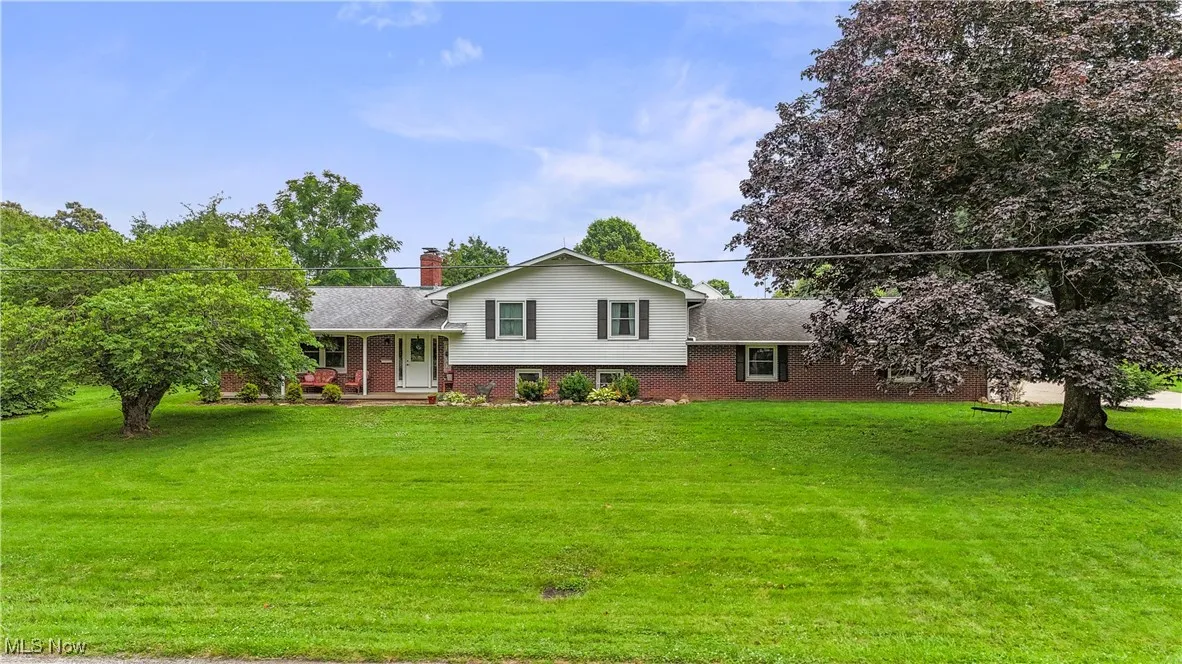 Tri-level home with a chimney, brick siding, covered porch, and a front yard