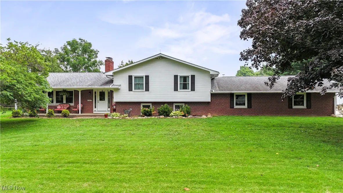 Tri-level home with brick siding, a shingled roof, a front lawn, and a chimney