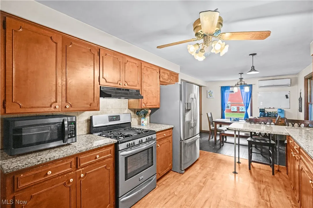 Kitchen featuring stainless steel appliances, ceiling fan, brown cabinetry, and backsplash