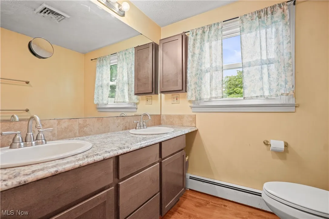 Full bathroom with baseboard heating, double vanity, and wood finished floors