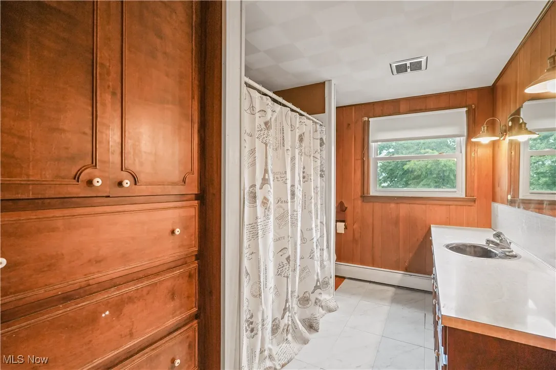 Full bath with vanity, wood walls, marble look tiles, a baseboard heating unit, and a shower with curtain