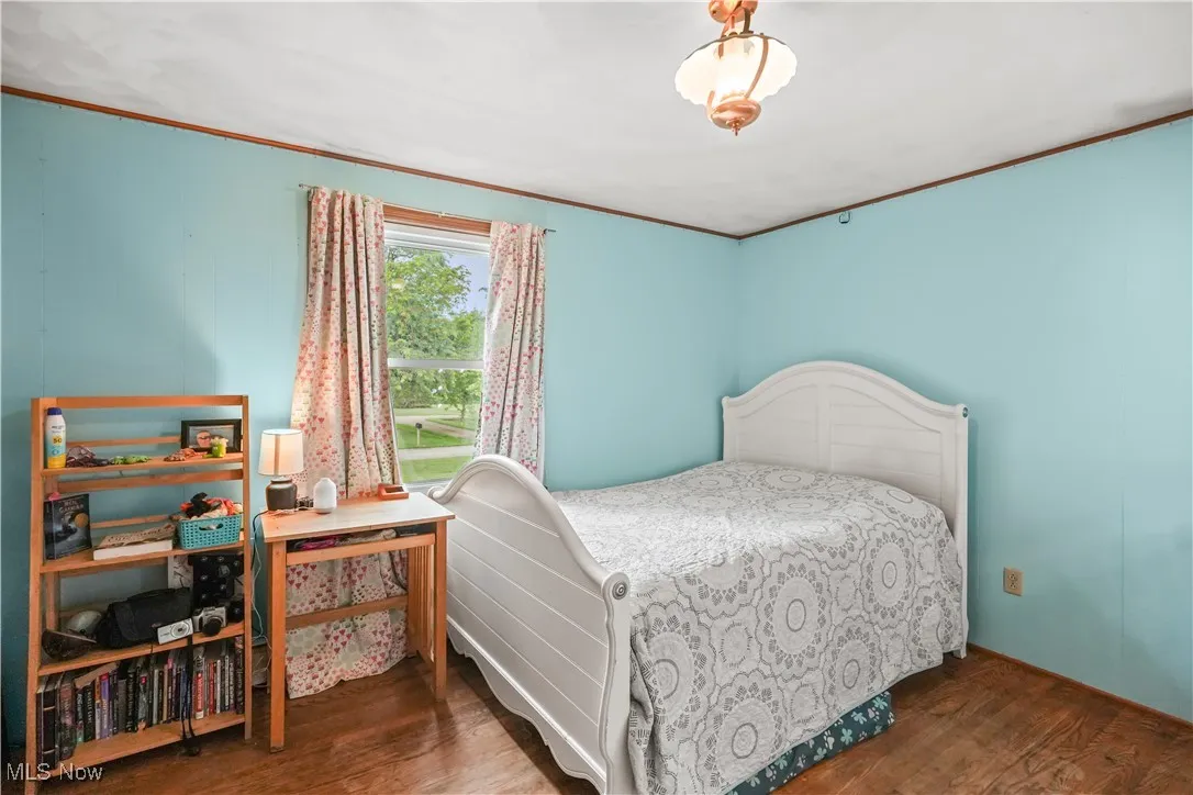 Bedroom with wood finished floors and ornamental molding