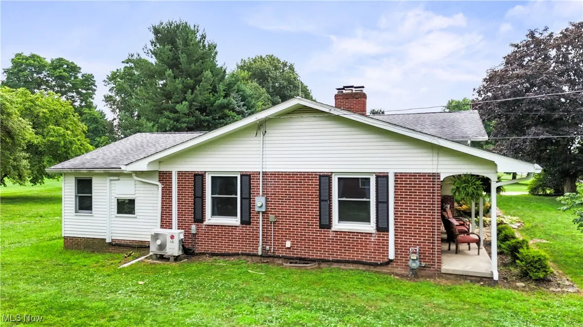 Rear view of property featuring roof with shingles, a yard, a chimney, and brick siding