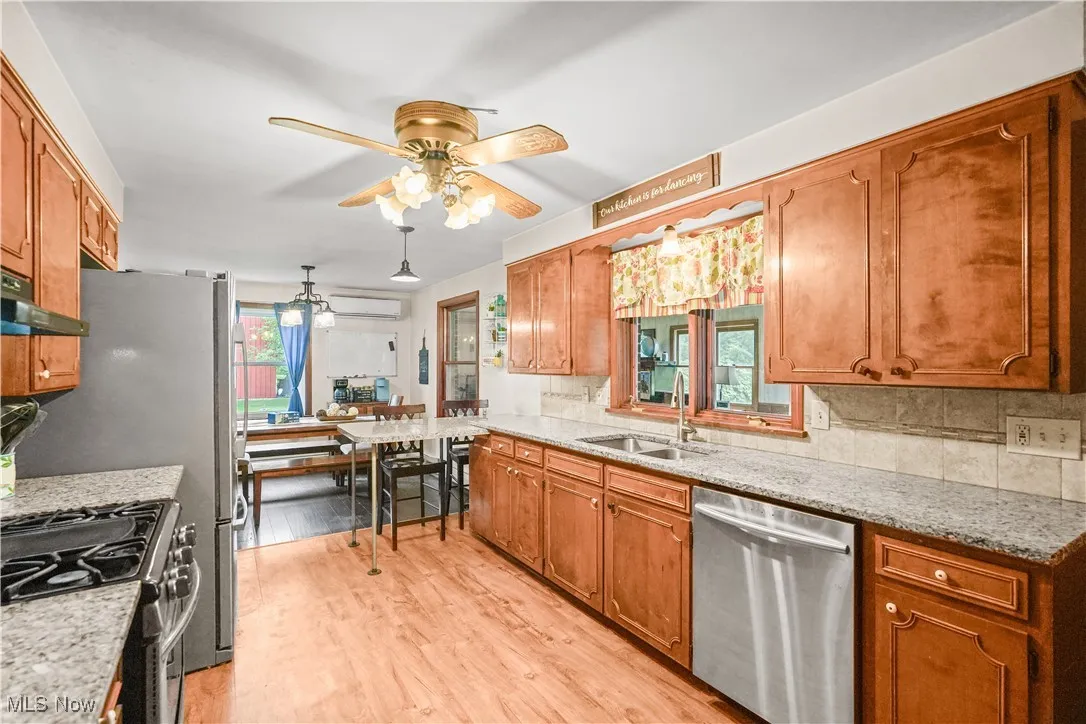 Kitchen with stainless steel appliances, decorative backsplash, light wood-style floors, ceiling fan, and brown cabinets