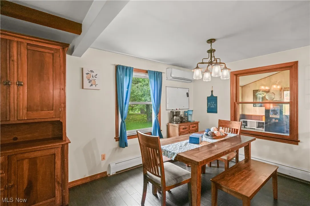 Dining space featuring a chandelier, a wall mounted AC, a baseboard heating unit, dark wood-style floors, and beamed ceiling