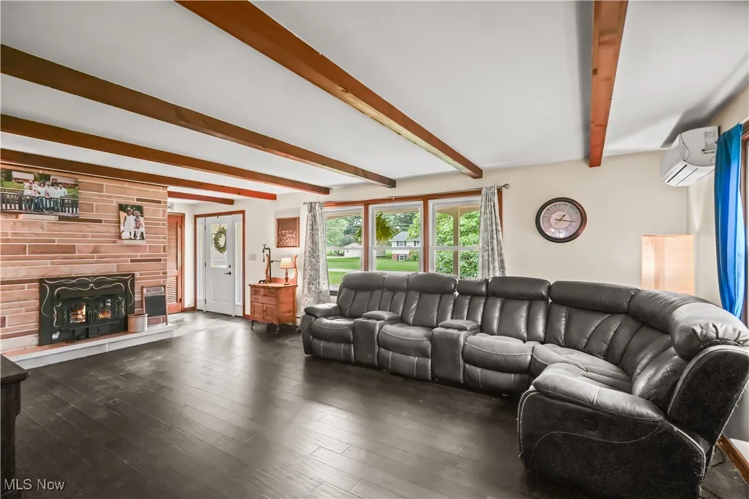 Living area featuring beamed ceiling, a wall mounted air conditioner, a warm lit fireplace, and wood finished floors