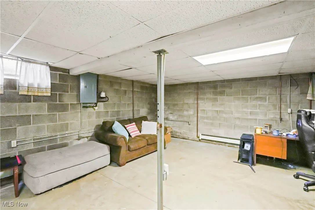 Below grade area featuring a drop ceiling, electric panel, and a baseboard heating unit