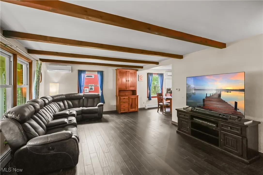 Living room with beamed ceiling, dark wood-style flooring, a wall mounted air conditioner, and a baseboard heating unit