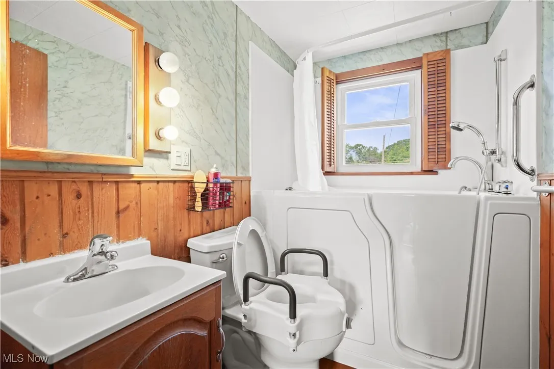 Full bathroom with vanity, wooden walls, and a bathtub