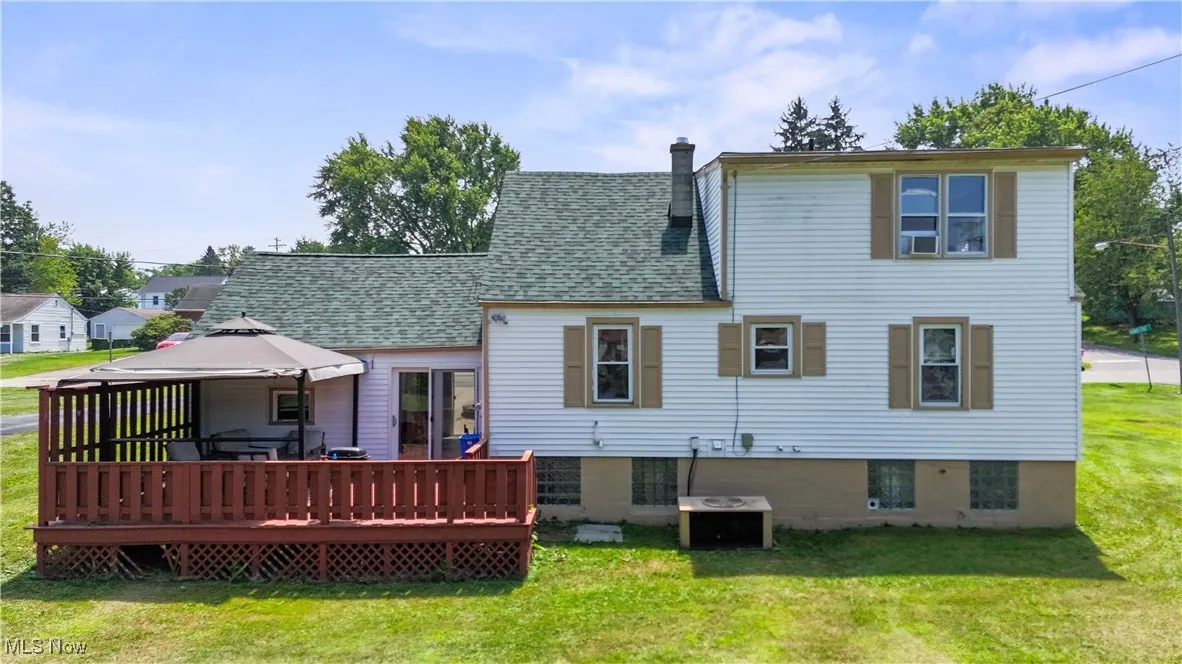 Rear view of house featuring a yard, a chimney, a deck, a gazebo, and roof with shingles