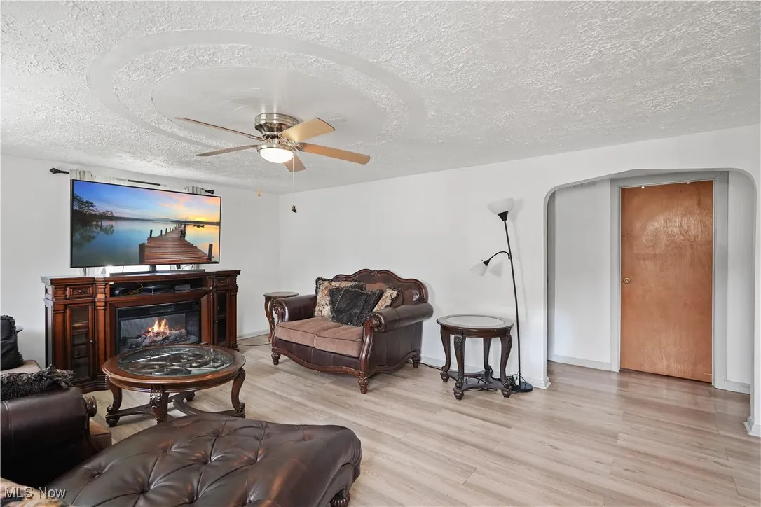 Living room with a textured ceiling, a ceiling fan, light wood-style floors, and a glass covered fireplace
