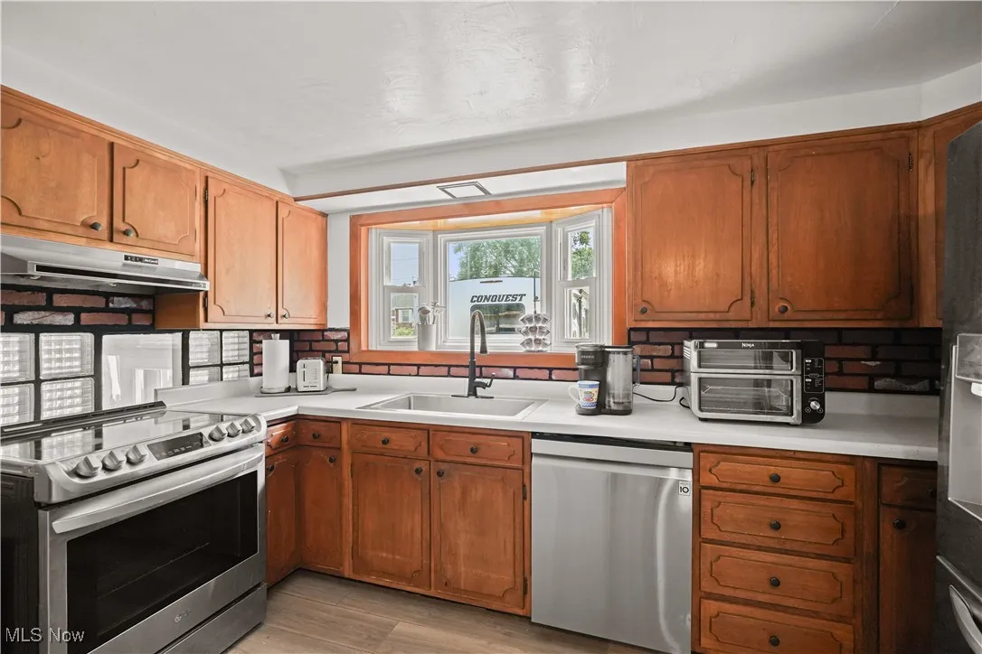 Kitchen with appliances with stainless steel finishes, under cabinet range hood, backsplash, and light countertops