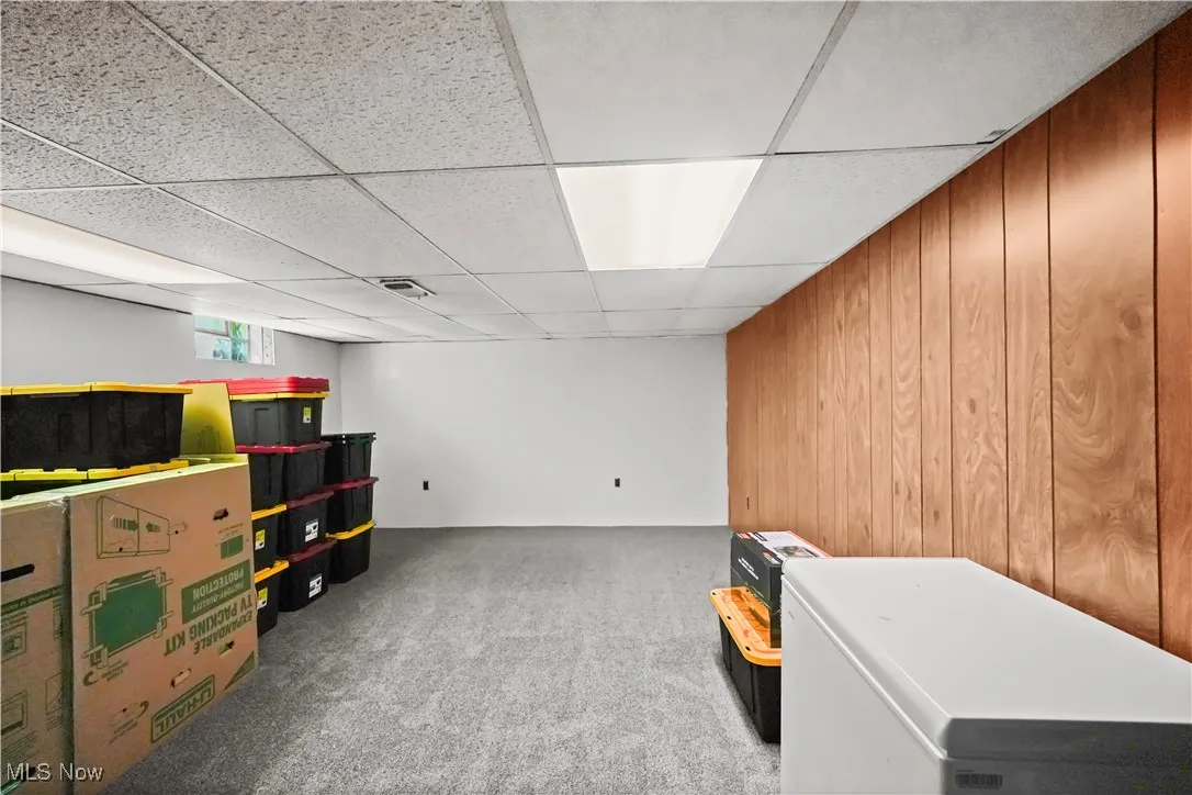 Basement featuring refrigerator, carpet floors, wood walls, and a drop ceiling