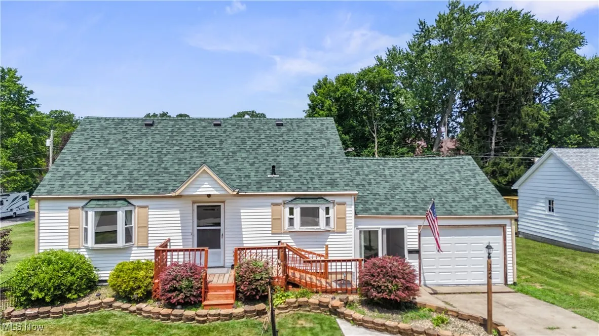 View of front of home with concrete driveway, a garage, a shingled roof, a deck, and a front lawn