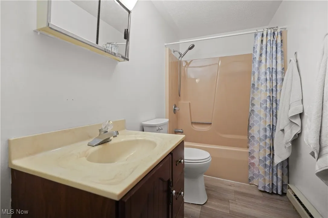 Full bath with vanity, a baseboard heating unit, shower / tub combo with curtain, wood finished floors, and a textured ceiling