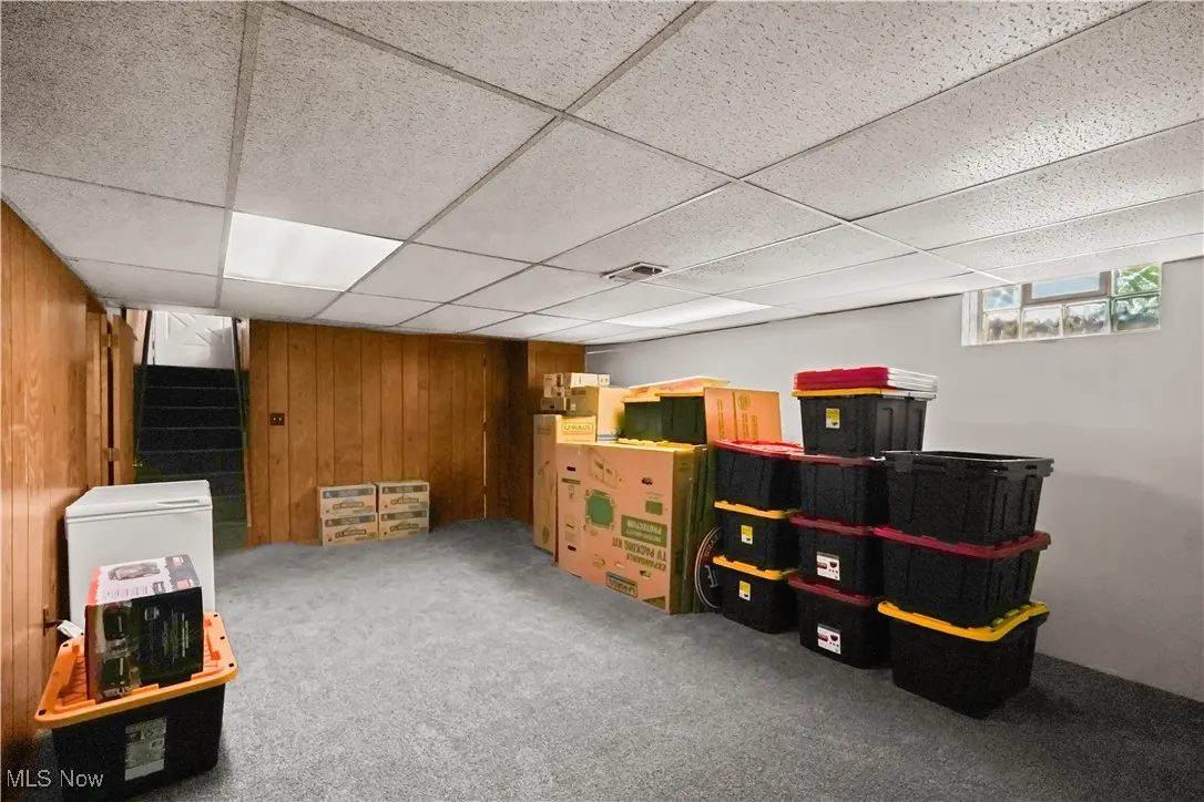 Below grade area featuring wooden walls, a drop ceiling, stairway, and carpet floors