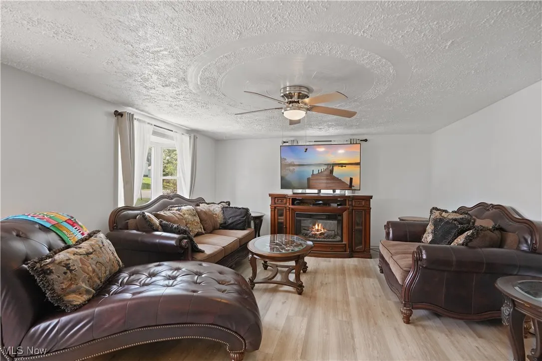 Living area featuring a textured ceiling, a ceiling fan, light wood-type flooring, and a glass covered fireplace