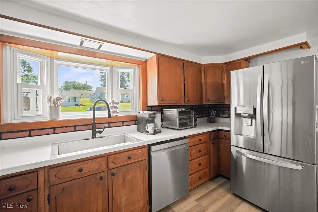 Kitchen featuring appliances with stainless steel finishes, brown cabinetry, light wood-type flooring, and light countertops