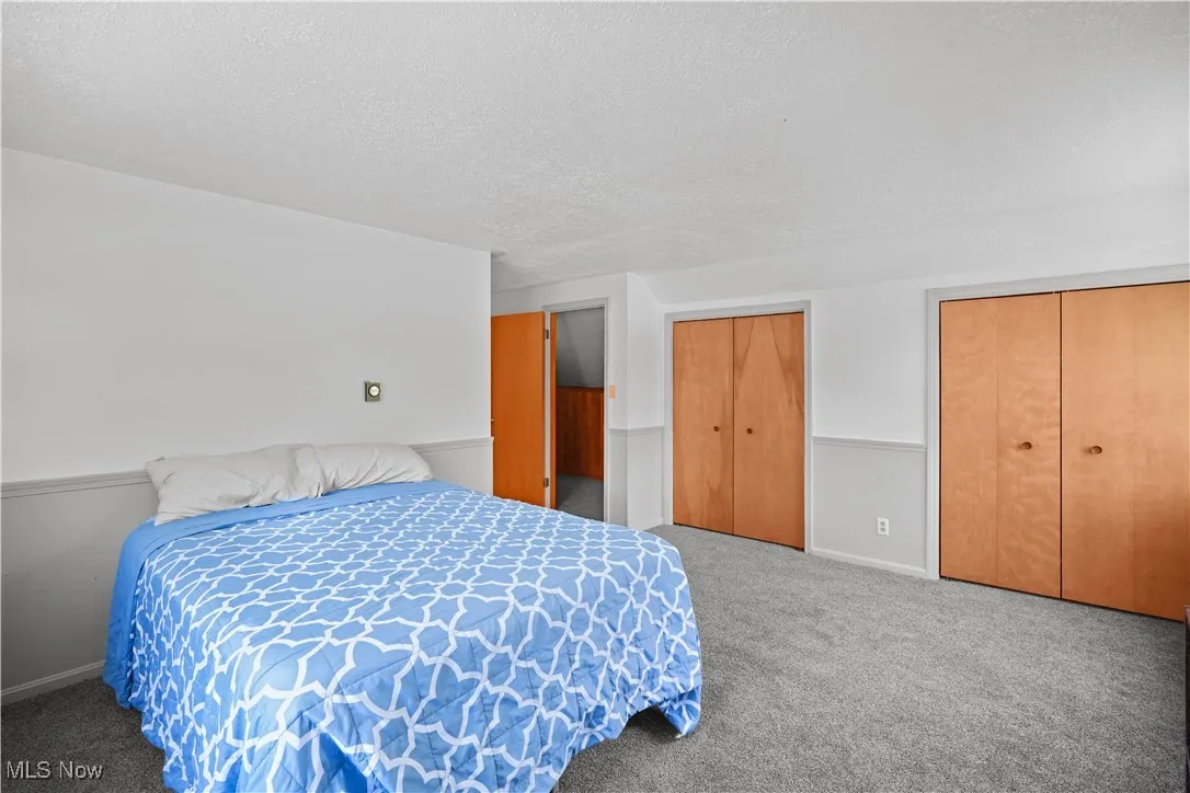 Bedroom with multiple closets, a textured ceiling, and carpet flooring