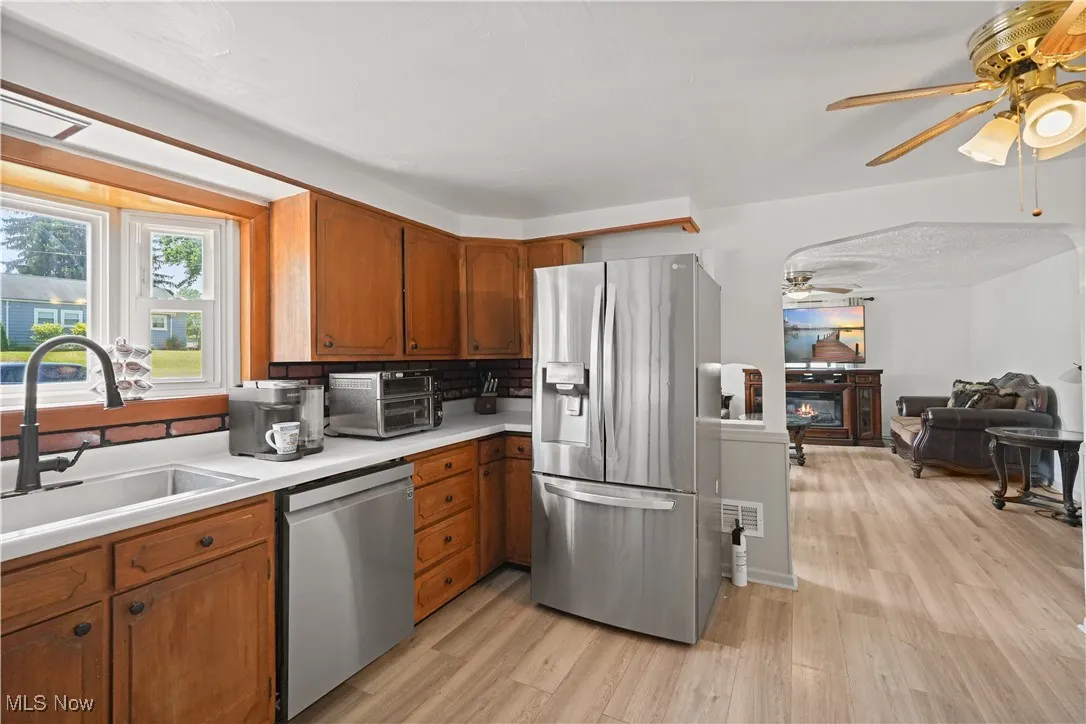 Kitchen with ceiling fan, stainless steel appliances, brown cabinets, light countertops, and light wood-style flooring