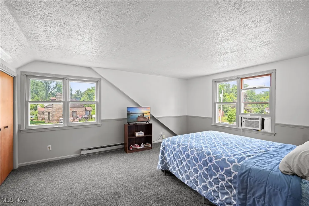 Bedroom featuring a textured ceiling, lofted ceiling, baseboard heating, carpet floors, and multiple windows