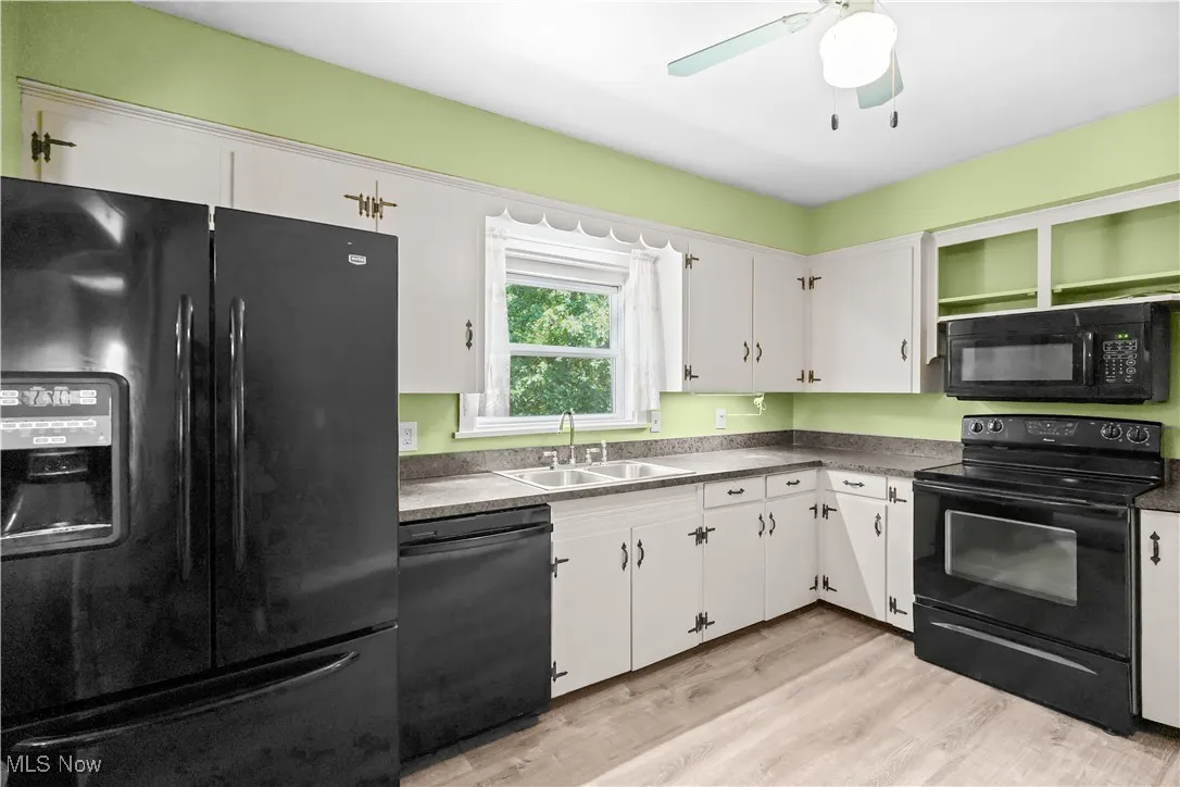 Kitchen with black appliances, white cabinetry, light wood-style floors, and dark countertops