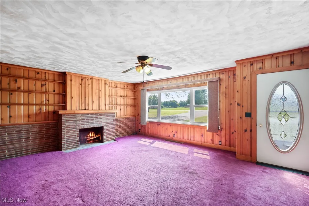 Unfurnished living room featuring wood walls, carpet, a fireplace, and a ceiling fan